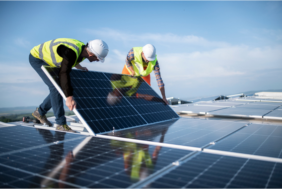 Dos trabajadores con casco sosteniendo un panel solar en un tejado