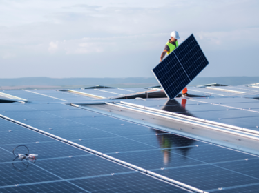 Trabajador con casco sosteniendo un panel solar en un tejado